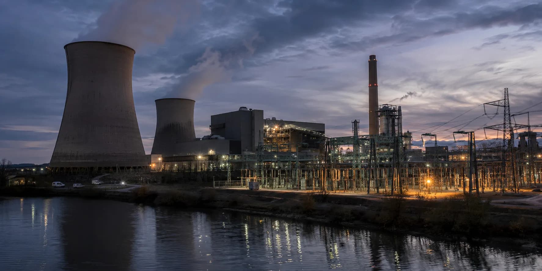 Power generation plant with cooling towers, electrical infrastructure and evening lighting